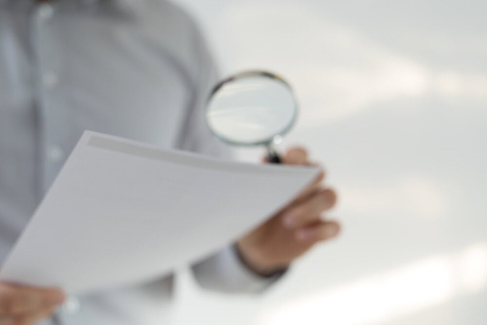 Man in a shirt with long sleeves looking at the papers through the magnifying glass Pharmacie, Ordonnance, ASAFO, Fraude, prescription, AmeliPro