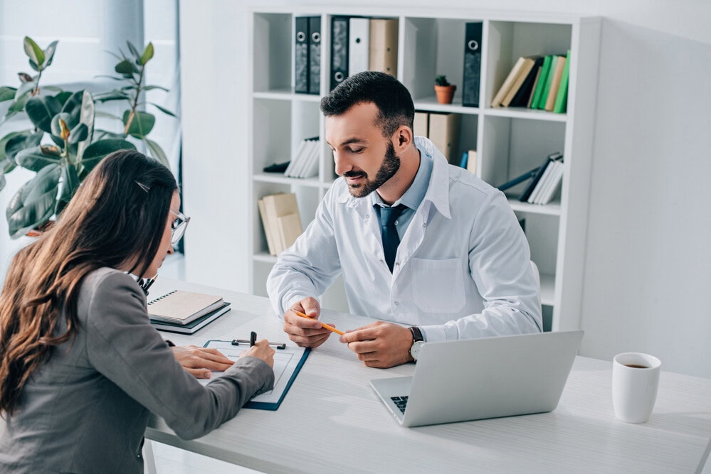 Patient signing insurance claim form near general practitioner in clinic