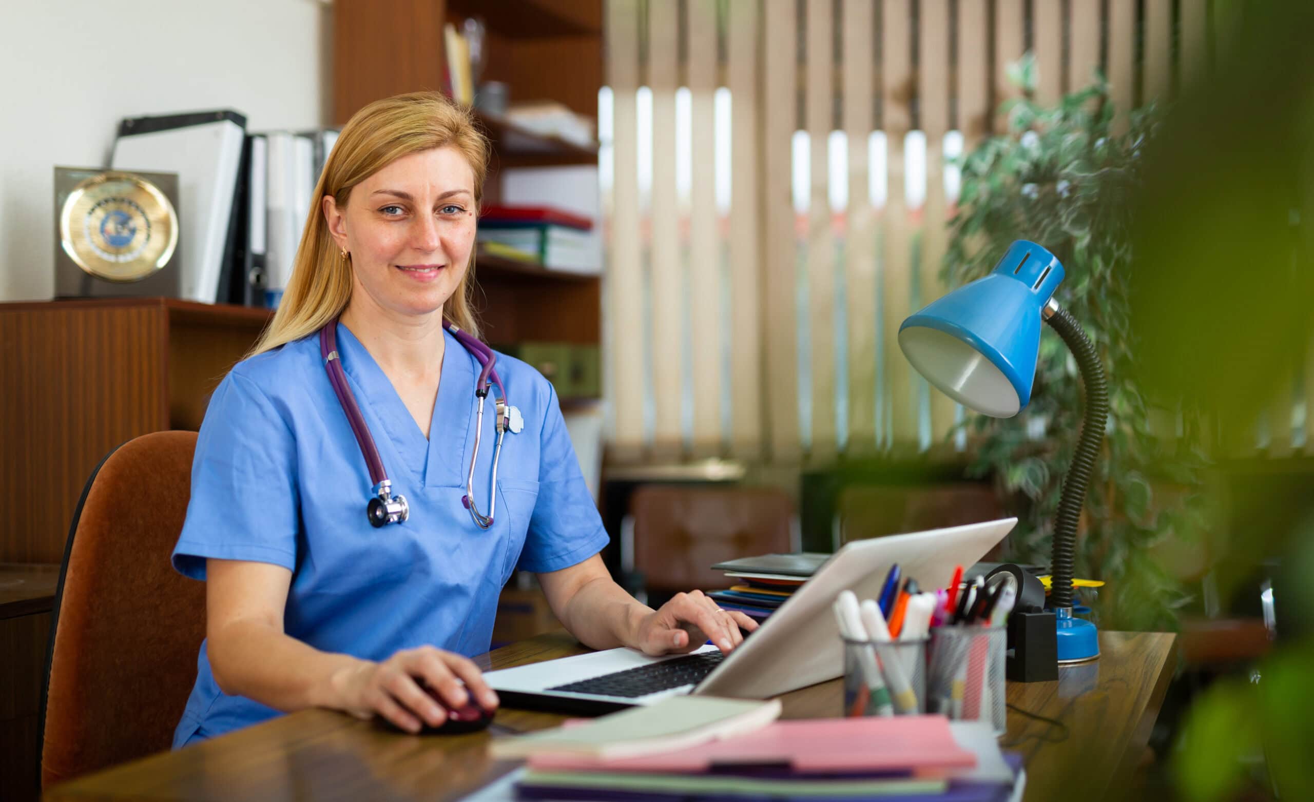 Positive woman doctor working in cabinet on laptop
