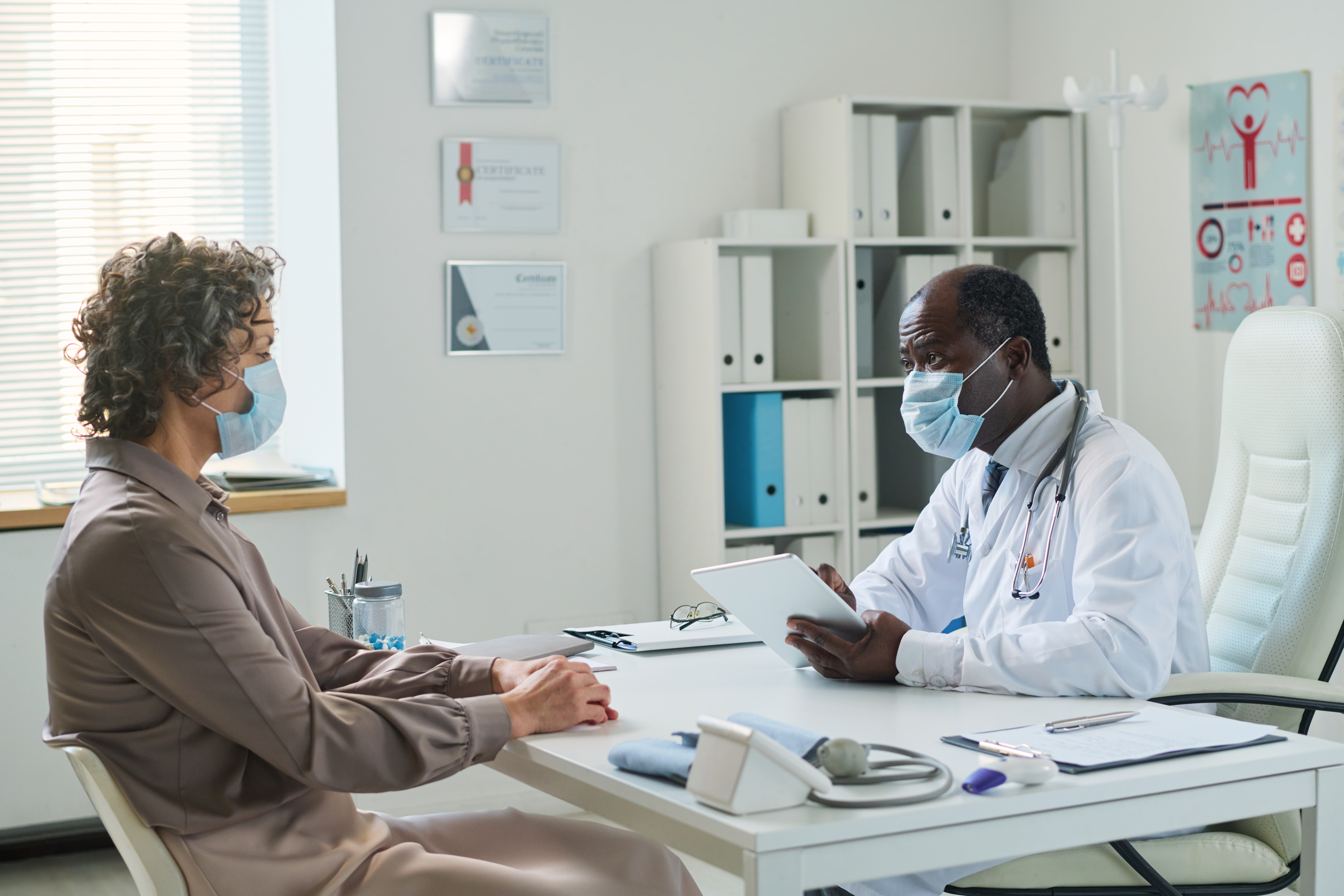 Experienced clinician with tablet and mature female patient wearing masks