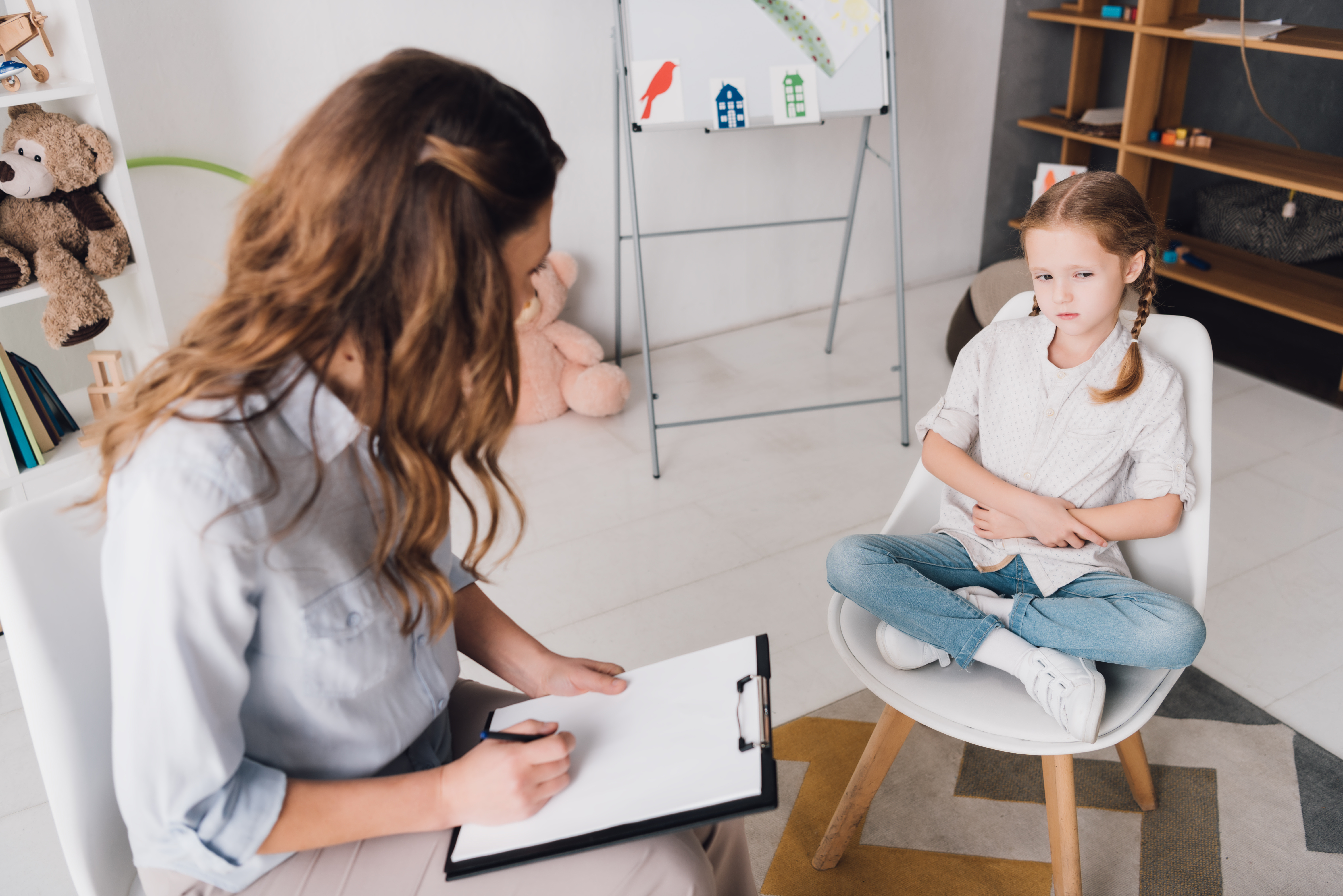 High angle view of psychologist with clipboard talking to little child in office